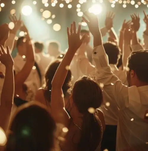 Menschen tanzen mit erhobenen Händen unter warmen, festlichen Lichtern, während ein DJ bei einer lebhaften Indoor-Feier in Berlin Musik auflegt.