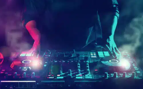 Ein DJ legt auf einem bunten, beleuchteten Plattenspieler in einer rauchigen, lebhaften Atmosphäre Musik auf.