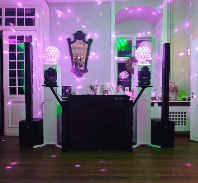 DJ-Pult mit Lautsprechern und bunten Disco-Lichtern in einem mit Spiegeln und Partydekorationen geschmückten Raum.